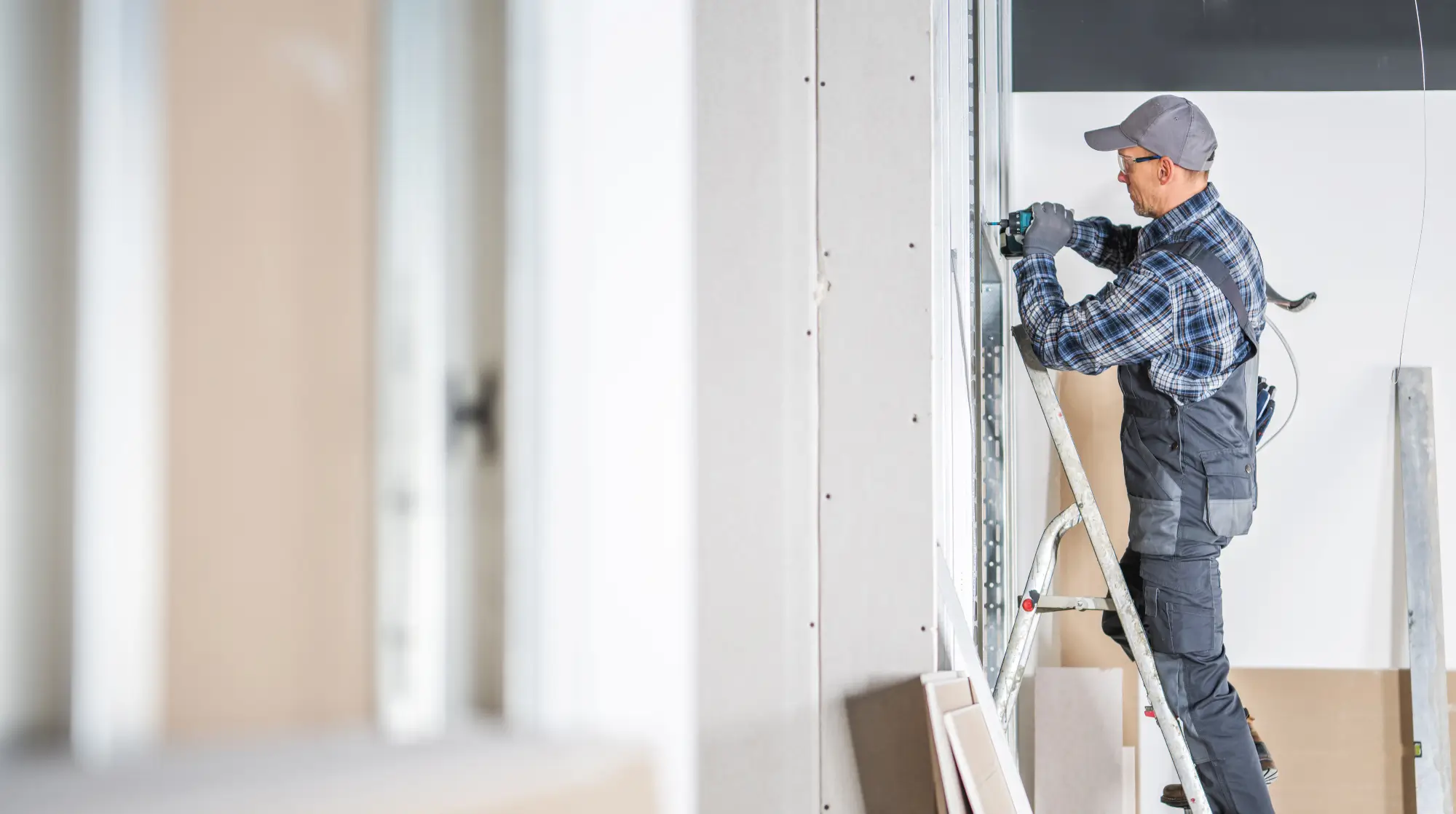 Professional drywall contractor installing drywall on a wall, using a power tool, showcasing precision and attention to detail in a clean workspace.