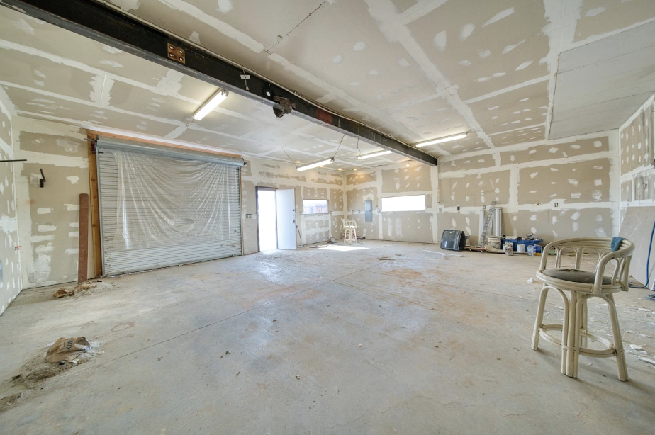 Empty garage space with unfinished drywall, visible lighting fixtures, and a chair, illustrating a project area for drywall installation and repair.